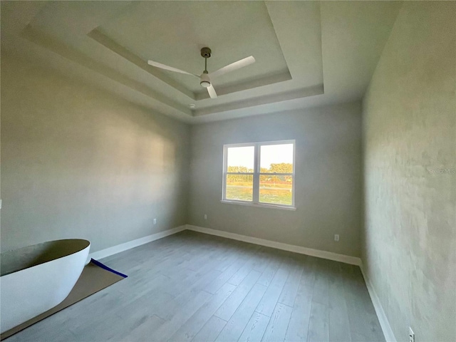 unfurnished room with a raised ceiling, light wood-type flooring, and ceiling fan