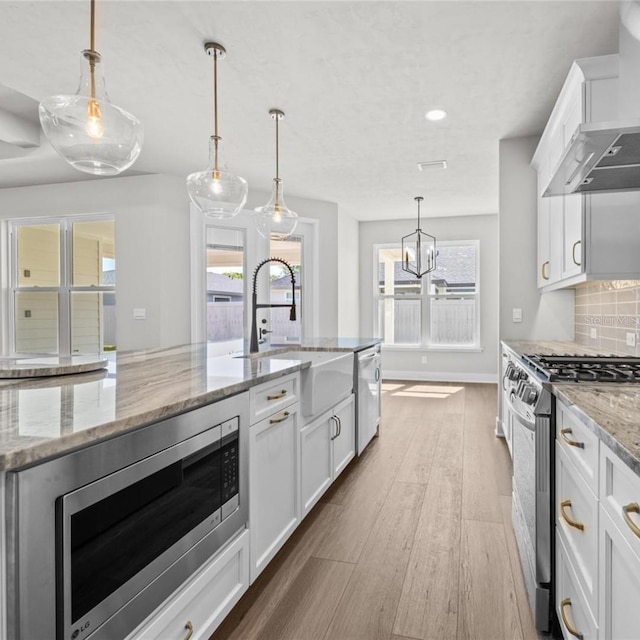 kitchen with white cabinetry, light stone countertops, stainless steel appliances, and light wood-type flooring