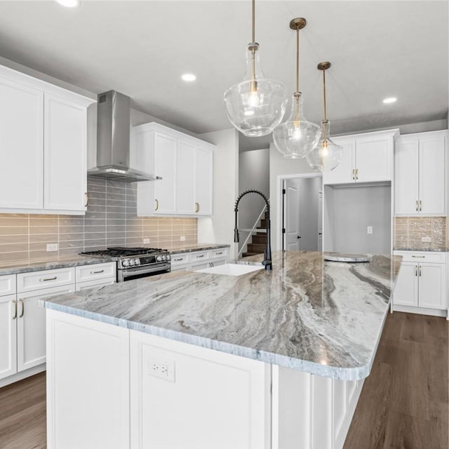 kitchen featuring a spacious island, white cabinetry, stainless steel stove, pendant lighting, and wall chimney exhaust hood