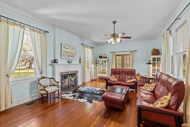 living room with ceiling fan, a textured ceiling, hardwood / wood-style flooring, a fireplace, and crown molding