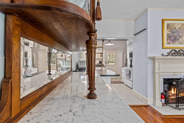 hall with a wealth of natural light, ornamental molding, ornate columns, and a textured ceiling