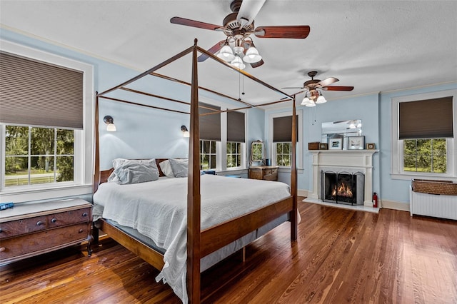 bedroom featuring hardwood / wood-style floors, multiple windows, radiator heating unit, and ceiling fan