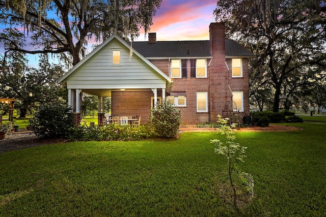 back house at dusk featuring a lawn