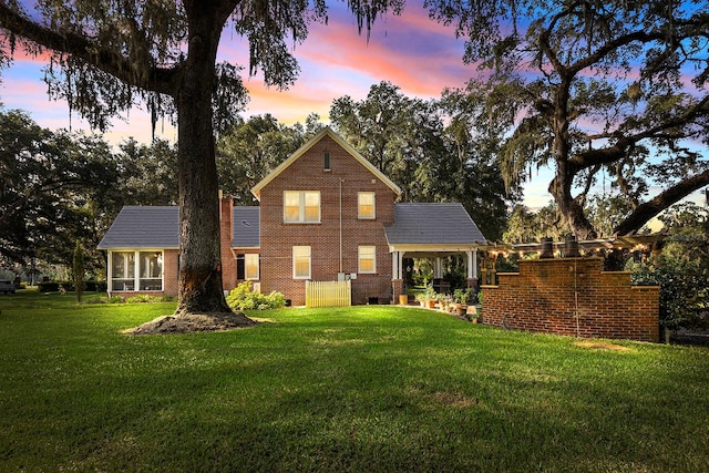 back house at dusk featuring a lawn