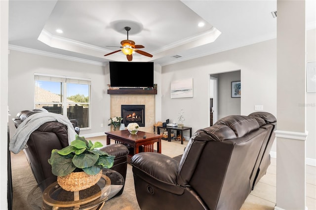 living room with crown molding, light tile patterned floors, a raised ceiling, a fireplace, and ceiling fan