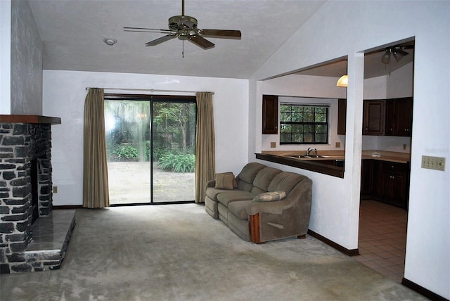 carpeted living room with a fireplace, vaulted ceiling, ceiling fan, and sink