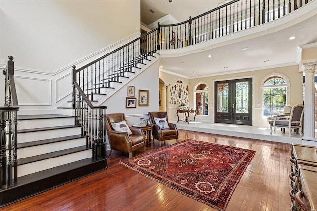 foyer featuring french doors, wood-type flooring, ornamental molding, decorative columns, and a towering ceiling