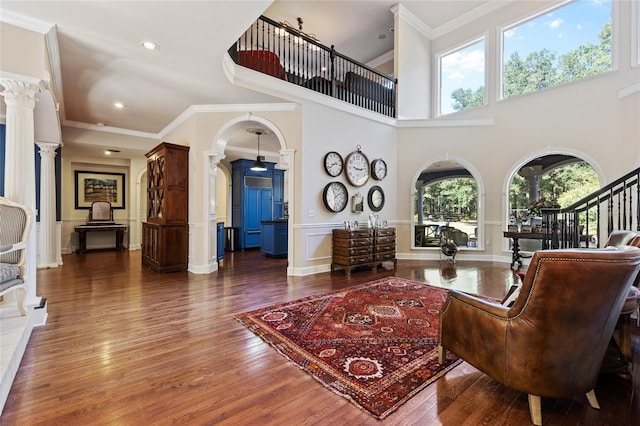 living room with a towering ceiling, ornamental molding, dark wood-type flooring, and decorative columns