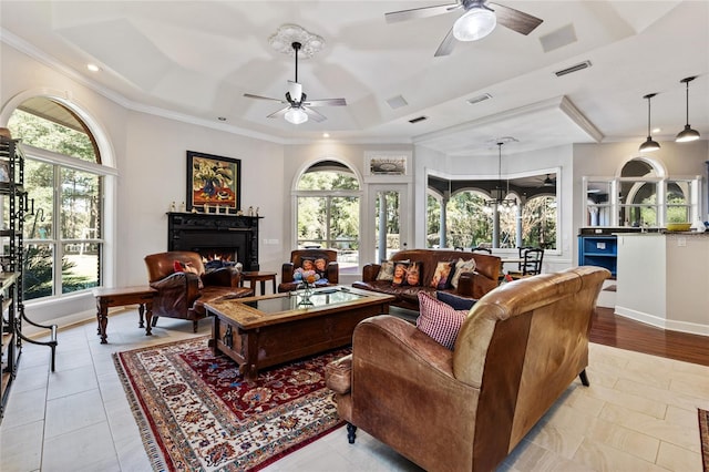 living room with a wealth of natural light, crown molding, ceiling fan with notable chandelier, and light tile patterned floors