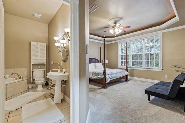 carpeted bedroom featuring sink, a textured ceiling, a tray ceiling, ceiling fan, and ornamental molding