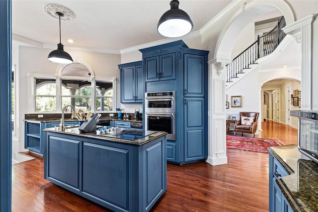 kitchen featuring stainless steel double oven, dark wood-type flooring, dark stone counters, decorative light fixtures, and blue cabinetry