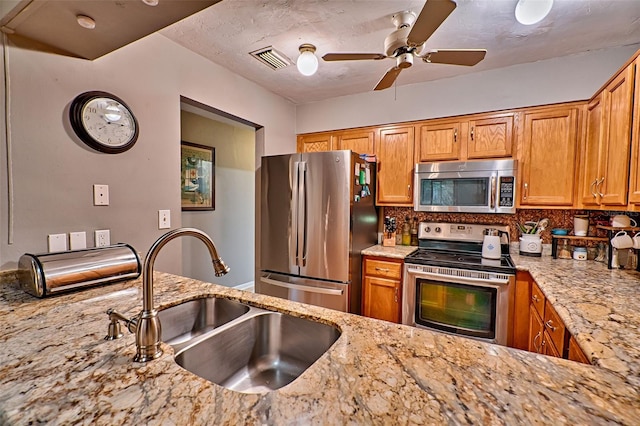 kitchen with sink, light stone countertops, stainless steel appliances, and tasteful backsplash