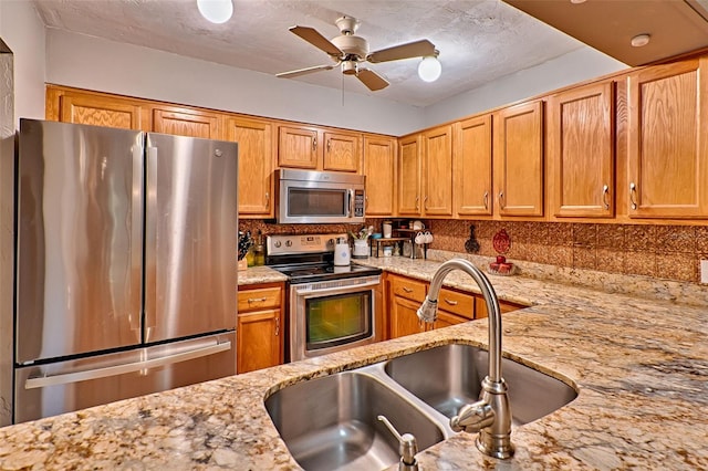 kitchen with light stone countertops, appliances with stainless steel finishes, sink, backsplash, and a textured ceiling