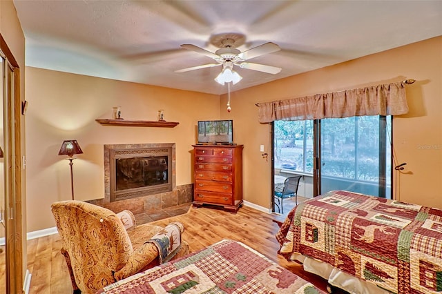 bedroom with access to outside, light hardwood / wood-style flooring, a fireplace, and ceiling fan