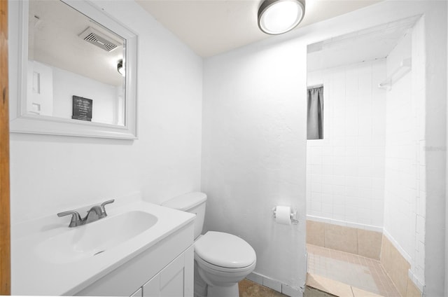 bathroom with vanity, a tile shower, toilet, and tile patterned floors