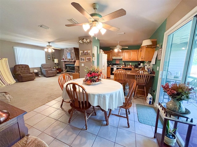 dining room with light colored carpet, a fireplace, and ceiling fan