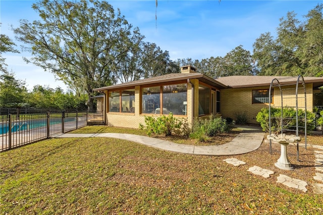 back of property with a sunroom, a fenced in pool, and a lawn