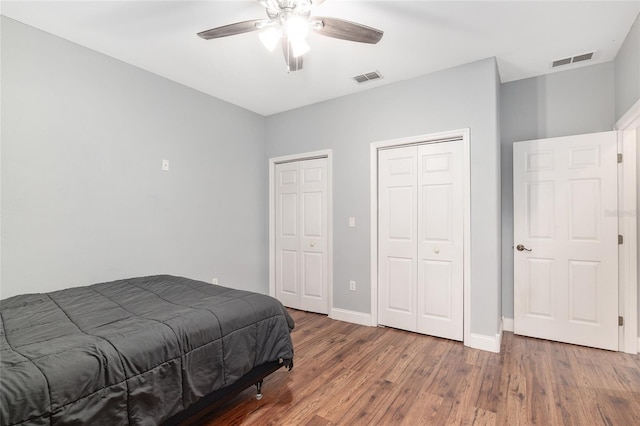 bedroom featuring dark hardwood / wood-style flooring, ceiling fan, and multiple closets