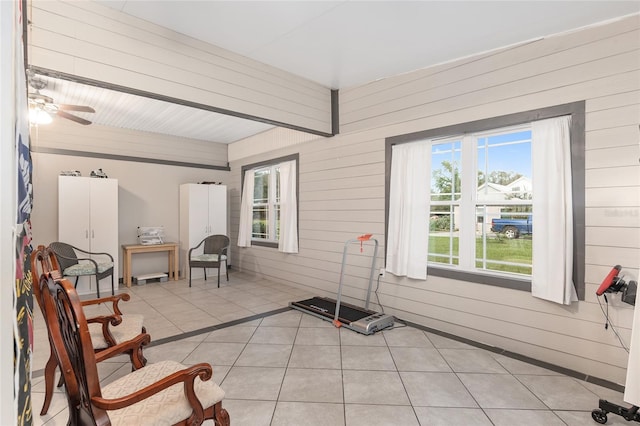 sitting room with wood walls, light tile patterned flooring, and ceiling fan