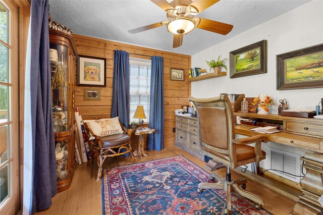 office area featuring ceiling fan, light hardwood / wood-style floors, a textured ceiling, and wood walls