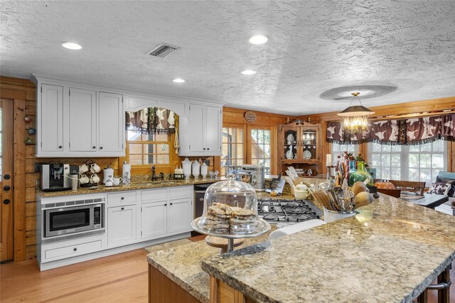 kitchen featuring stainless steel microwave, sink, white cabinets, light stone counters, and light hardwood / wood-style floors