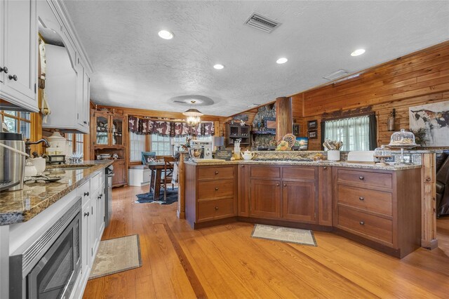 kitchen featuring wood walls, a textured ceiling, light hardwood / wood-style flooring, stainless steel microwave, and white cabinets