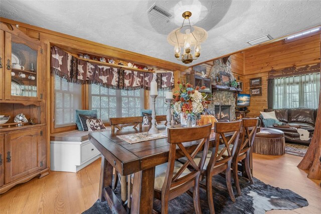 dining area with an inviting chandelier, a textured ceiling, light hardwood / wood-style flooring, and wood walls