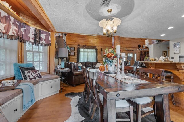 dining area with a chandelier, a textured ceiling, light hardwood / wood-style floors, and wood walls