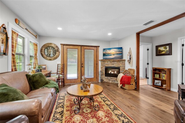 living room with french doors, a stone fireplace, and light hardwood / wood-style flooring