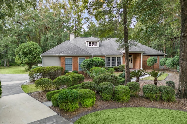 view of front of property with roof with shingles, brick siding, a chimney, and a front yard