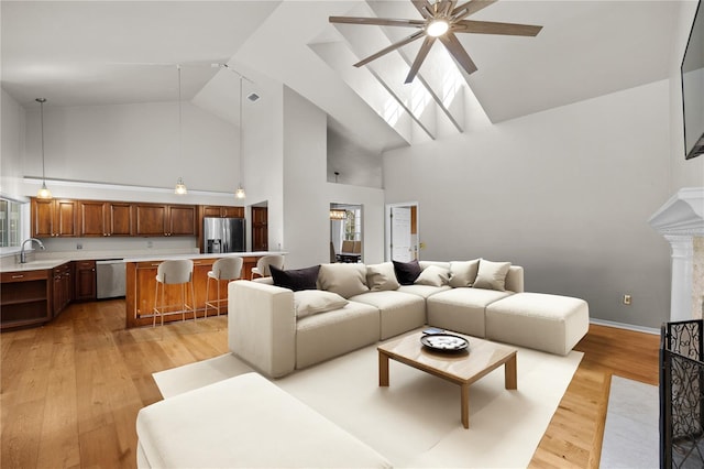 living area featuring high vaulted ceiling, light wood-style flooring, a skylight, visible vents, and baseboards