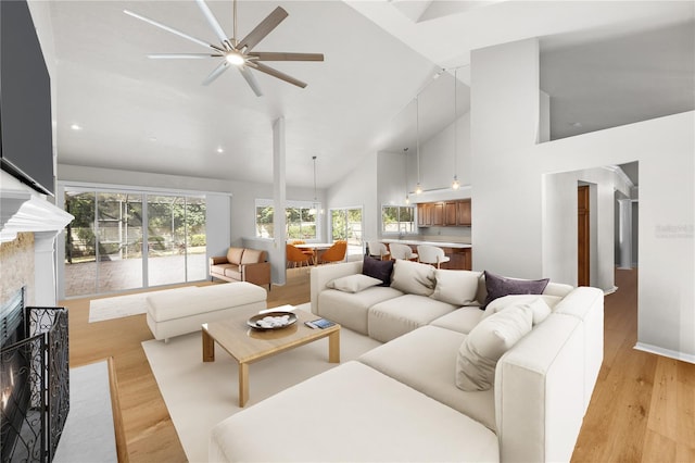 living room featuring ceiling fan, high vaulted ceiling, light wood finished floors, and a fireplace