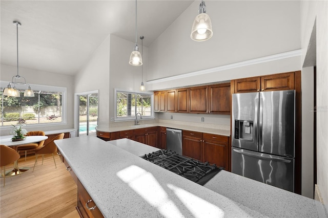 kitchen featuring stainless steel appliances, a sink, hanging light fixtures, light stone countertops, and light wood finished floors