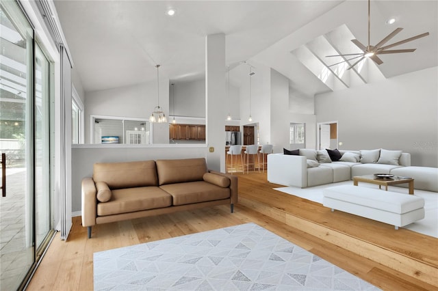 living area with high vaulted ceiling, light wood-type flooring, and a skylight