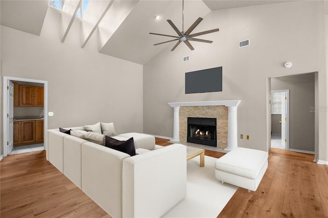 living room with visible vents, a ceiling fan, a fireplace with flush hearth, light wood-type flooring, and high vaulted ceiling