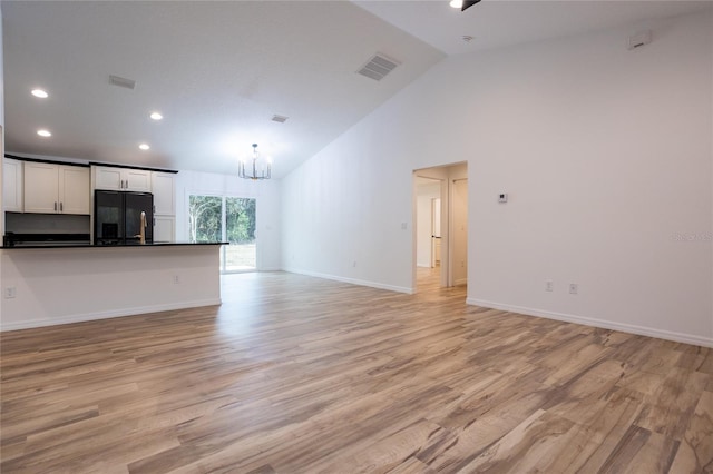 unfurnished living room featuring a notable chandelier, light hardwood / wood-style flooring, and high vaulted ceiling