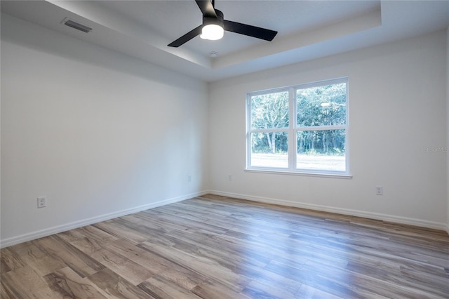 unfurnished room with ceiling fan, light hardwood / wood-style flooring, and a tray ceiling