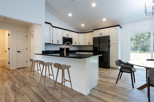 kitchen with light wood-style floors, dark countertops, a peninsula, black appliances, and a kitchen bar