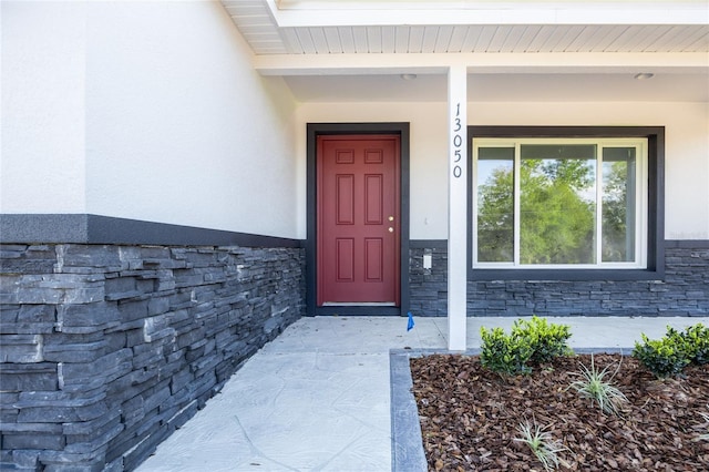 doorway to property featuring stone siding, covered porch, and stucco siding