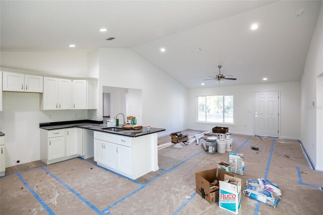 kitchen featuring a peninsula, a sink, white cabinets, open floor plan, and dark countertops