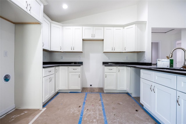 kitchen with dark countertops, recessed lighting, white cabinets, vaulted ceiling, and a sink