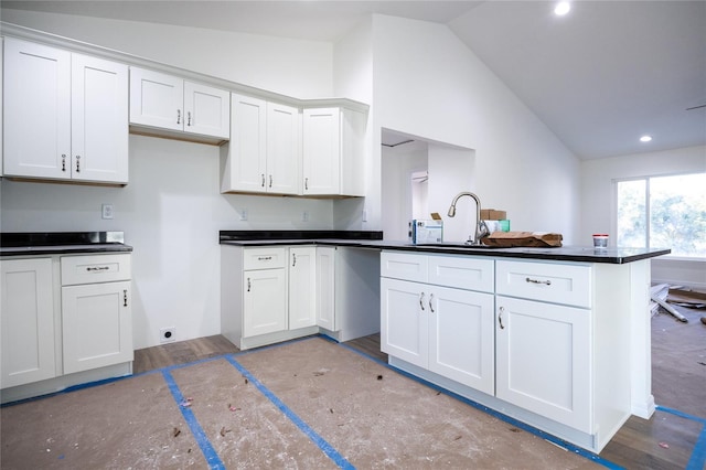 kitchen featuring dark countertops, white cabinets, vaulted ceiling, a sink, and a peninsula