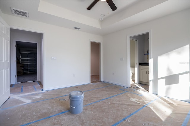 unfurnished bedroom featuring ensuite bathroom, a tray ceiling, visible vents, and baseboards