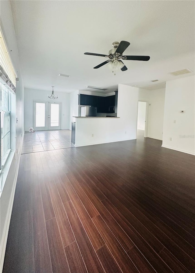 unfurnished living room featuring french doors, ceiling fan with notable chandelier, and dark wood-type flooring