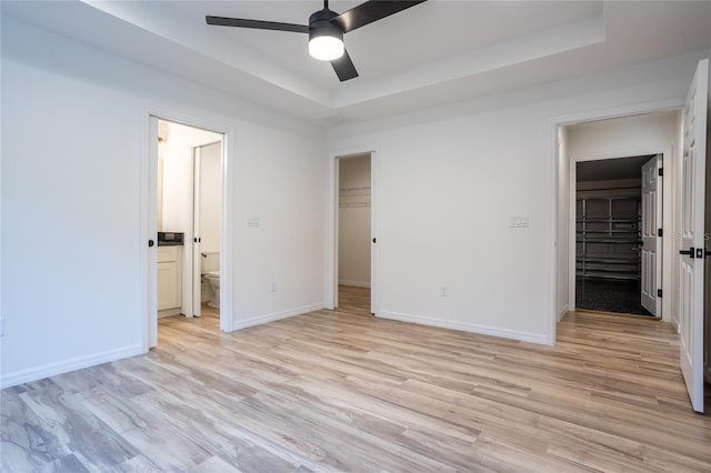 unfurnished bedroom with ceiling fan, a walk in closet, a closet, and a tray ceiling