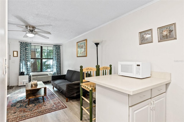 living room featuring a wall mounted AC, ornamental molding, light wood-type flooring, a textured ceiling, and ceiling fan