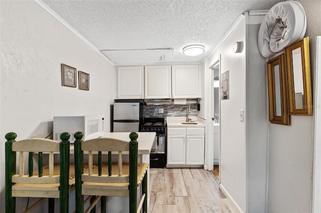 kitchen featuring sink, black range, backsplash, white cabinetry, and stainless steel fridge