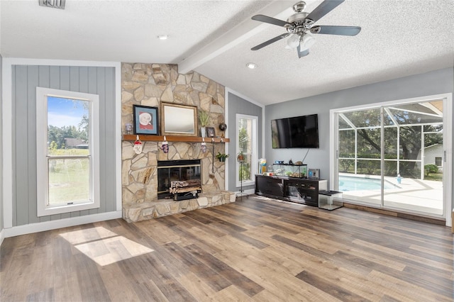 unfurnished living room featuring wood-type flooring, a healthy amount of sunlight, a stone fireplace, and lofted ceiling with beams