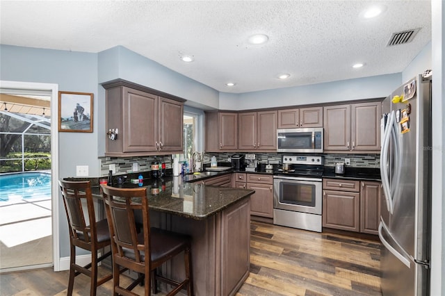 kitchen with kitchen peninsula, appliances with stainless steel finishes, a kitchen breakfast bar, tasteful backsplash, and dark hardwood / wood-style floors