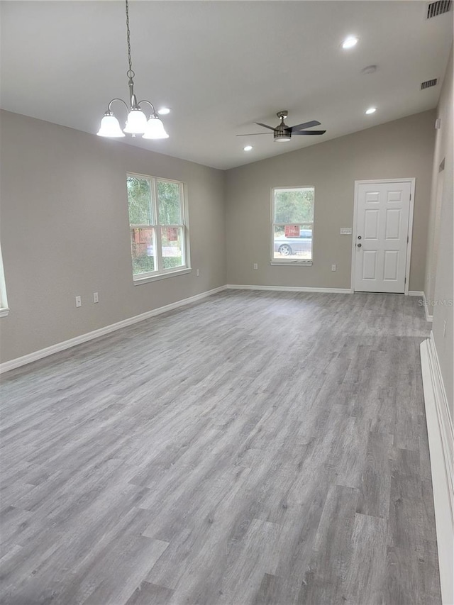 empty room with light wood-type flooring, a wealth of natural light, lofted ceiling, and ceiling fan with notable chandelier